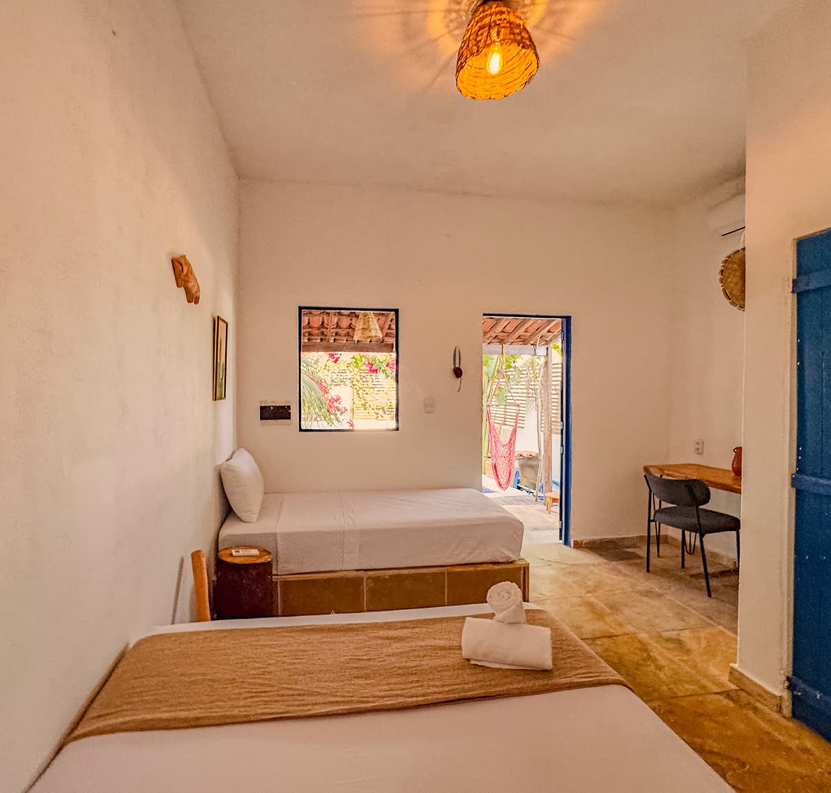 Cama de casal e cama de solteiro na Suíte Sertão, com porta azul e janela para o jardim da Casa Mareser