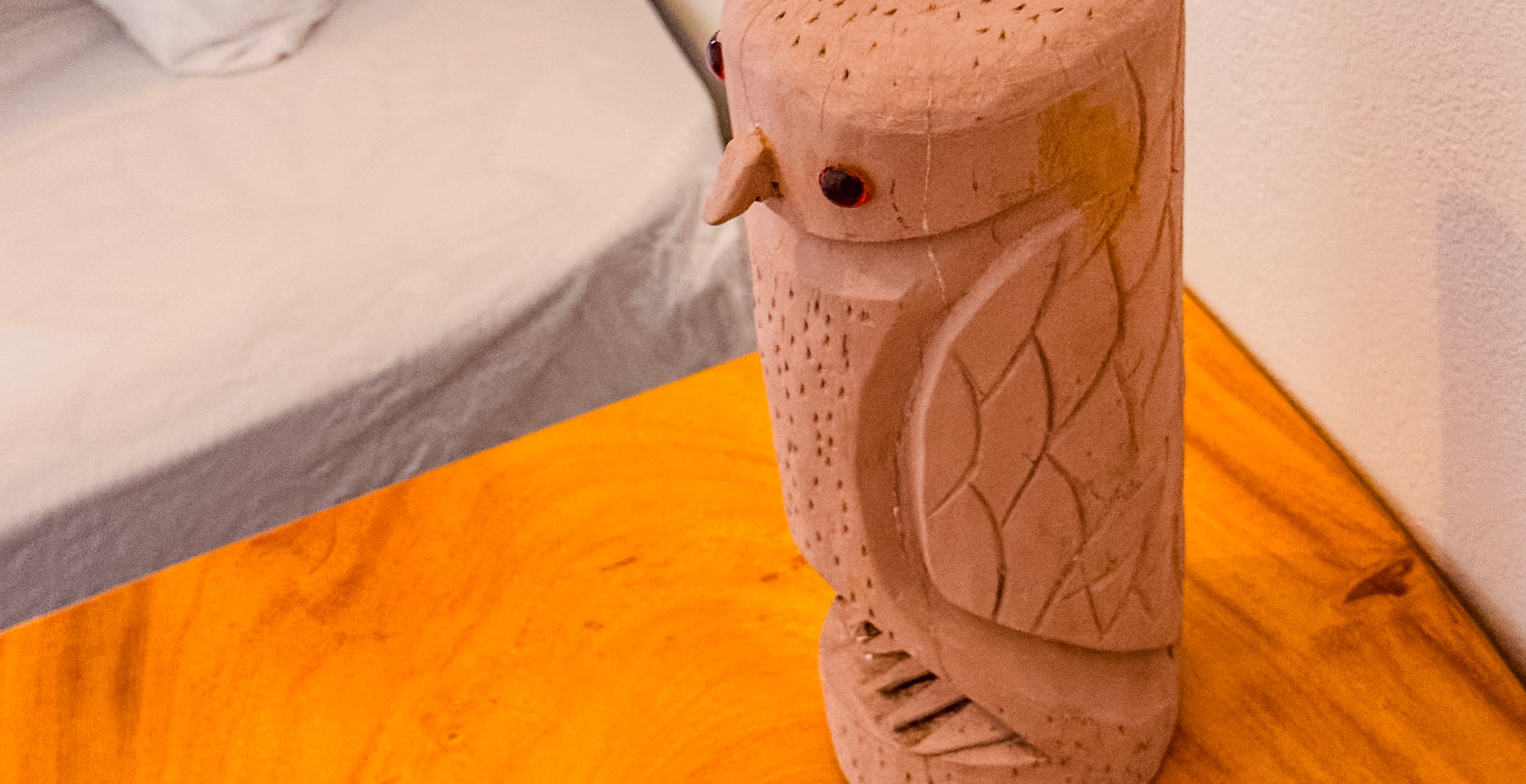 Detalhe de escultura artesanal de coruja em madeira sobre criado-mudo em uma suíte da Casa Mareser