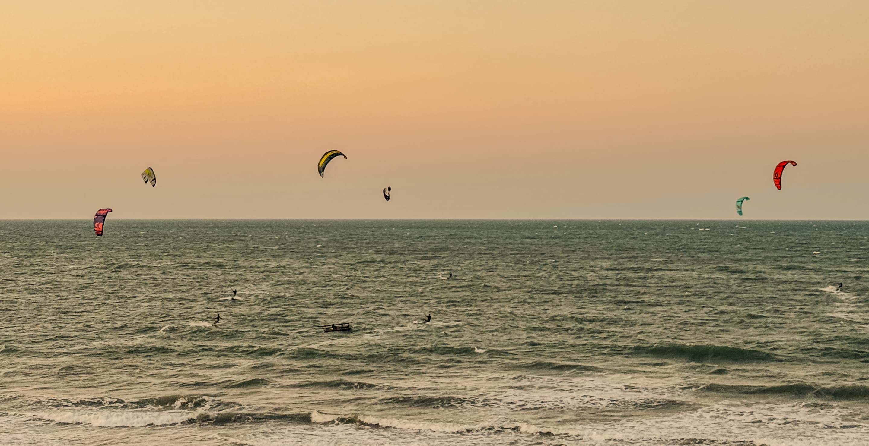 Praia com coqueiros e surfistas caminhando pela areia ao entardecer