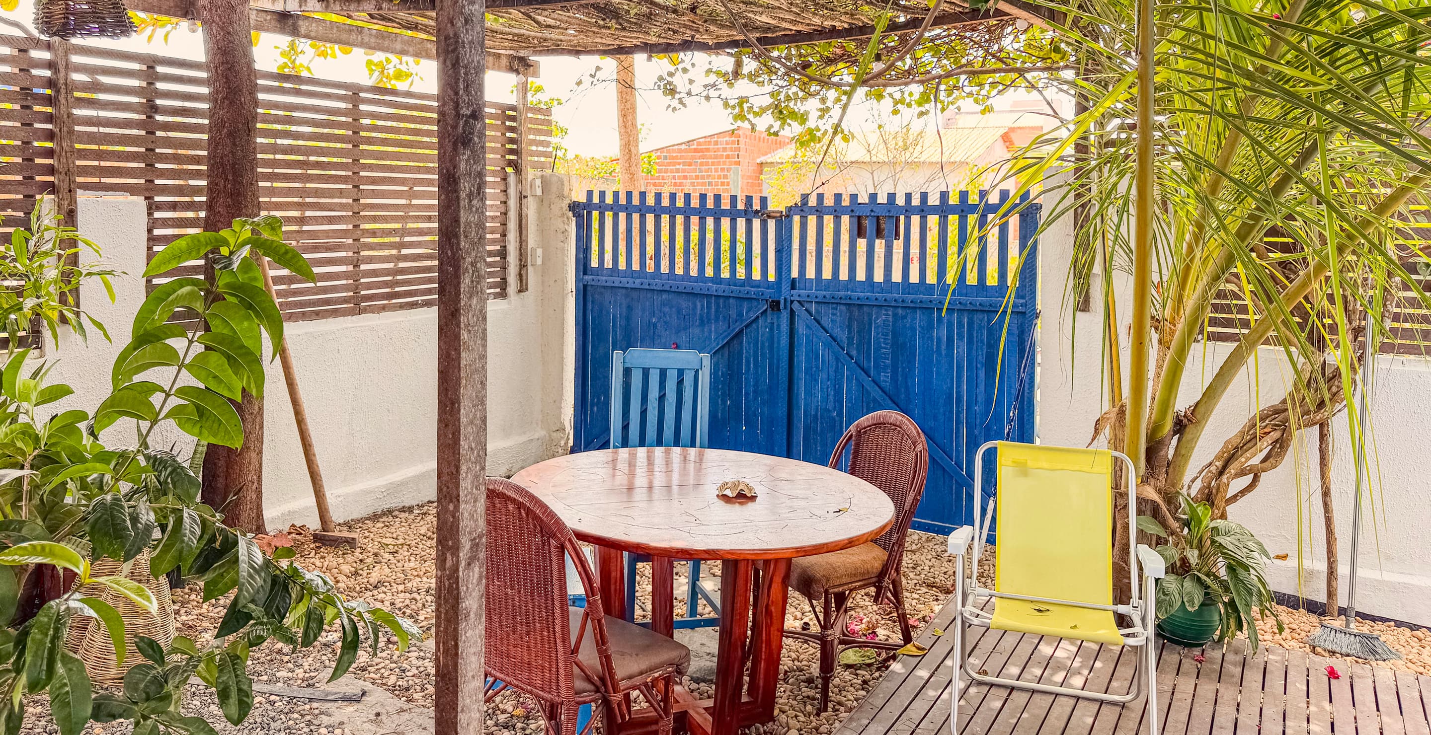 Área externa da Casa Mareser com mesa, cadeiras e portão azul sob pergolado